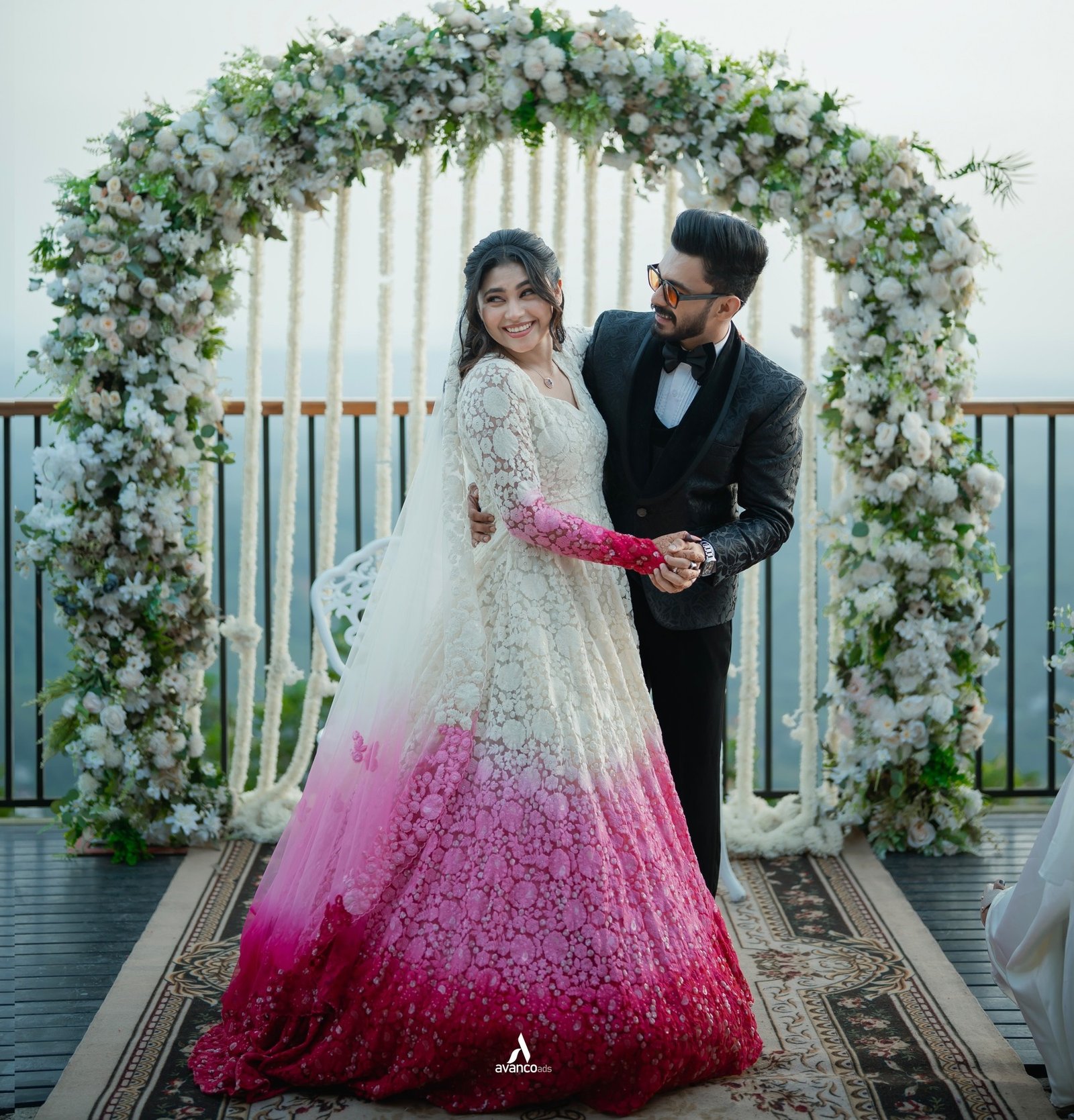 A bride and groom posing together beneath a floral arch