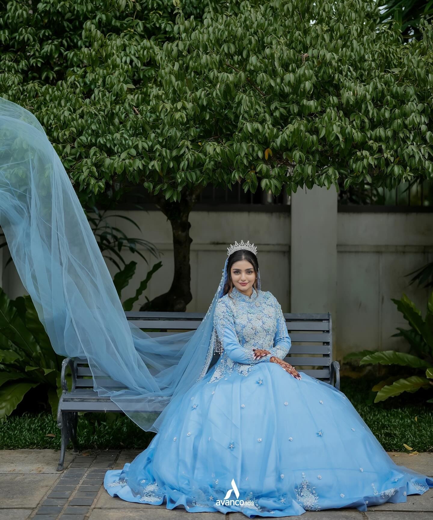 A bride seated in a garden with her veil flowing beside her